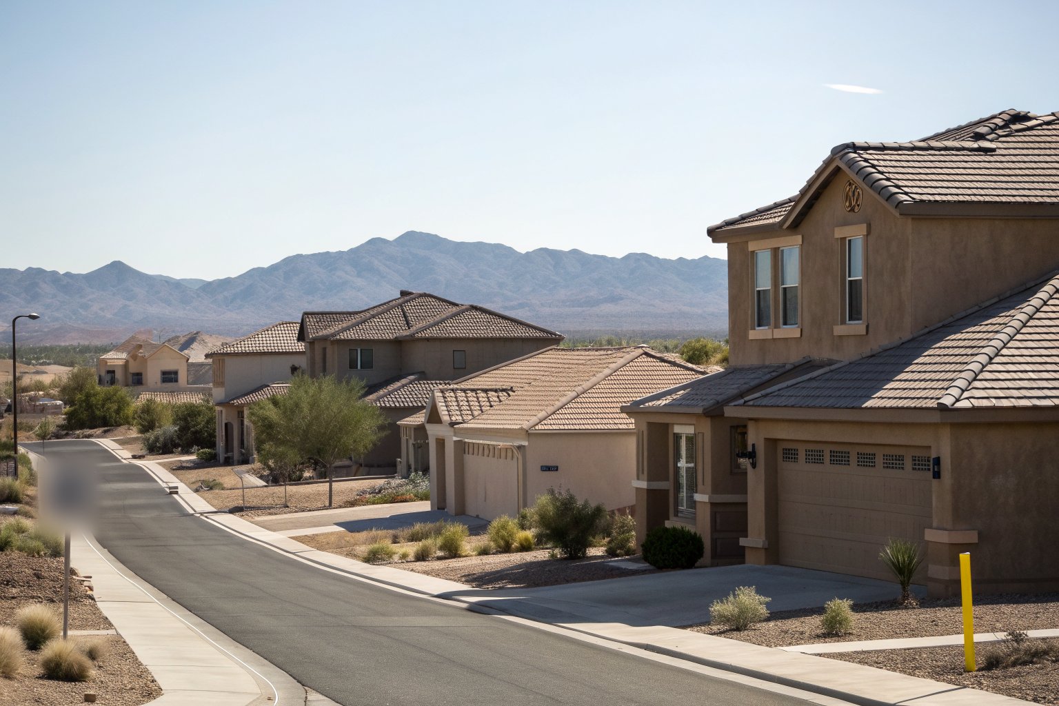 A street of newer stucco homes with brown concrete tile roofs and desert front yards, mountains on the horizon